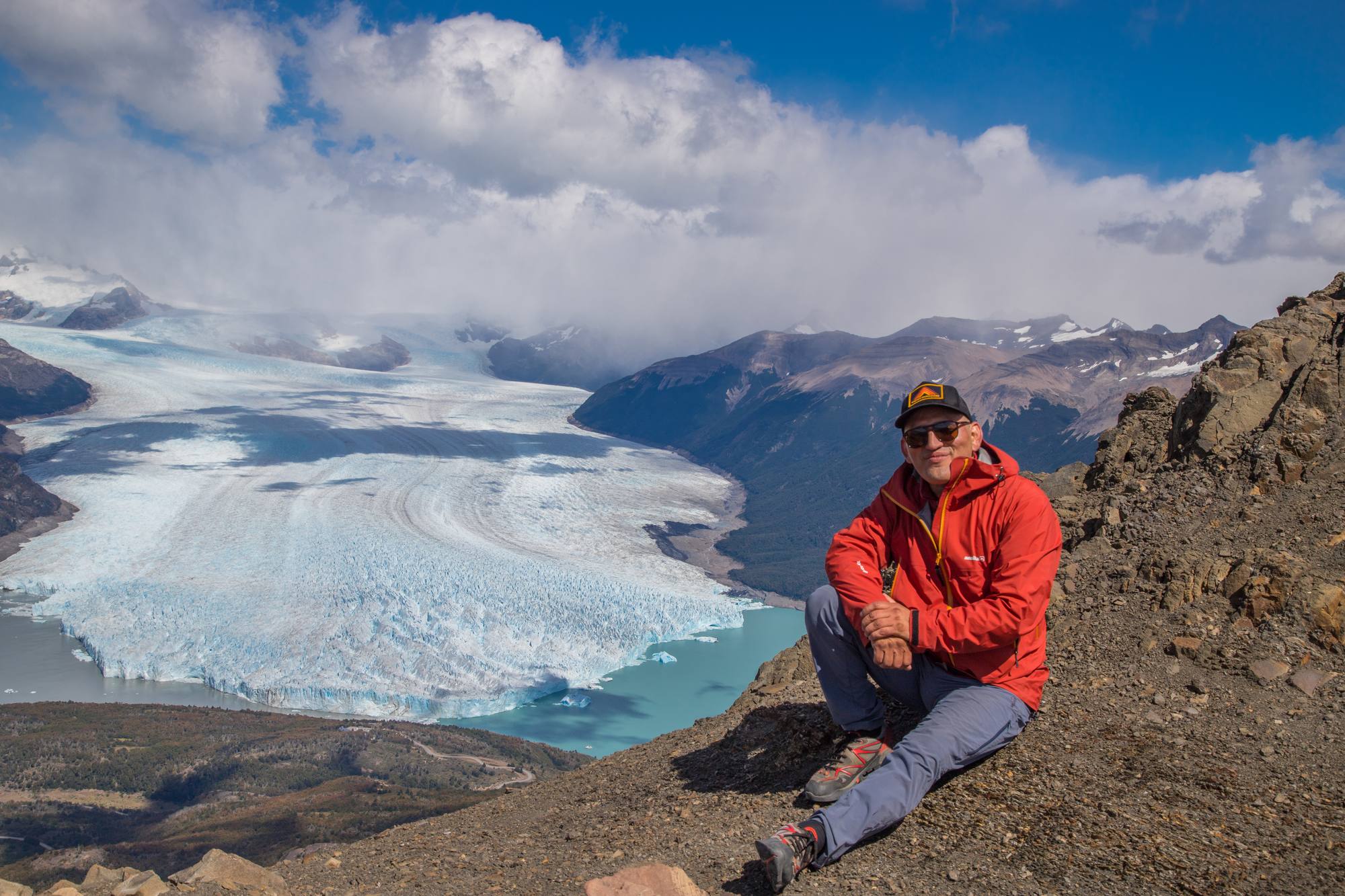 Luis Acharez sentado sobre una ladera frente al glaciar Perito Moreno y el Lago Argentino