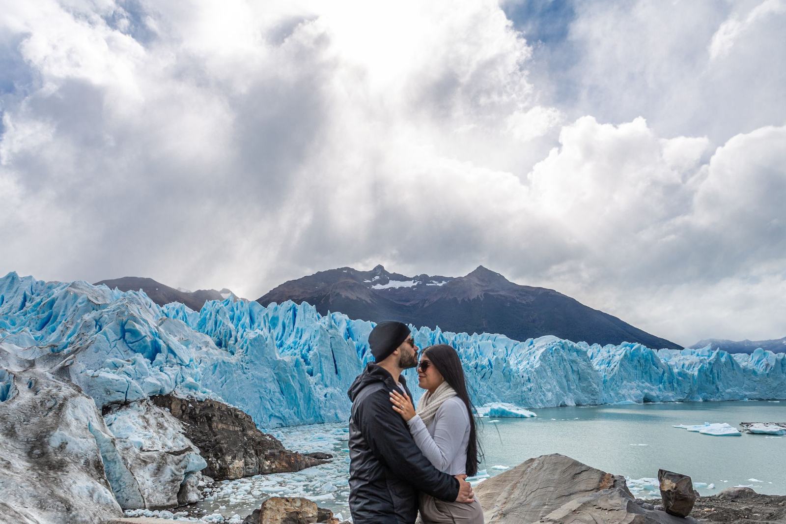 Una pareja abrazada sobre la nieve, con el glaciar Perito Moreno y el Lago Argentino detrás