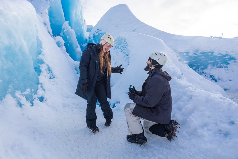 Un hombre con casco y grampones se arrodilla sobre el glaciar para proponer casamiento