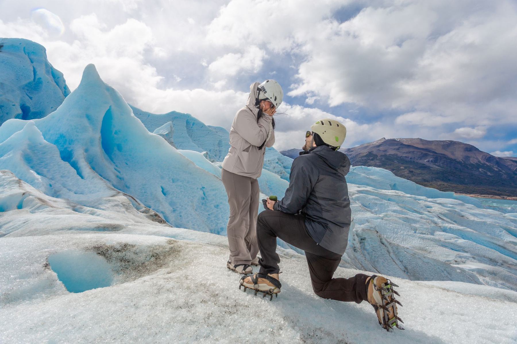 Un hombre de rodillas sobre el hielo del glaciar propone casamiento y ella se lleva las manos a la boca